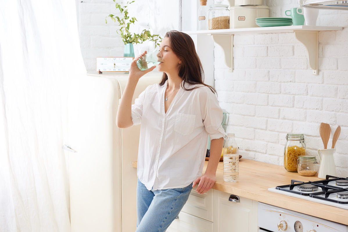 Frau in weißer Bluse trinkt ein Glas Wasser